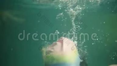 戴着游泳帽的女孩在水面上吸起空气，潜入水中。 少女在水下潜水。 录像